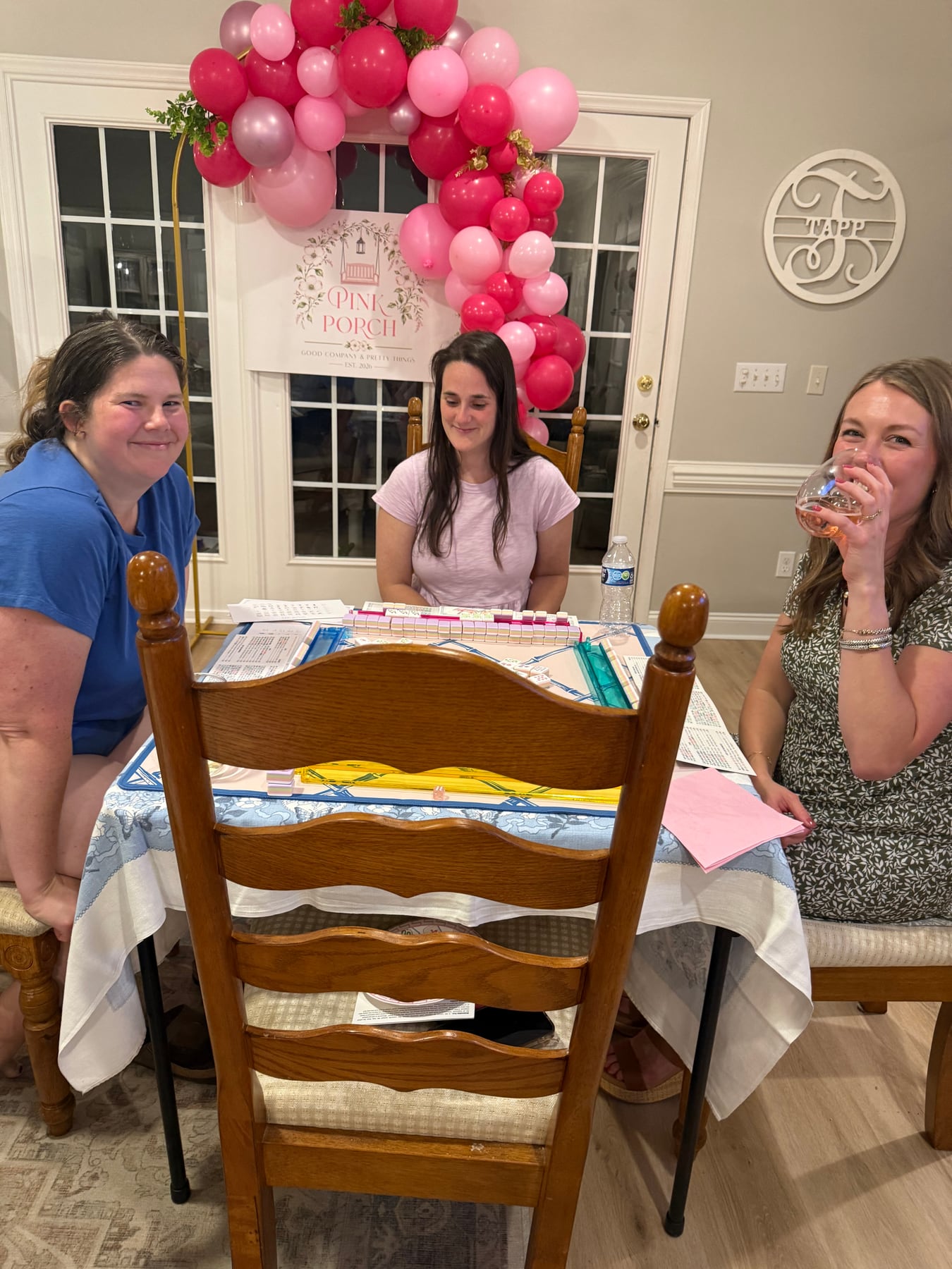Friends learning Mahjong together beneath a Pink Porch balloon display